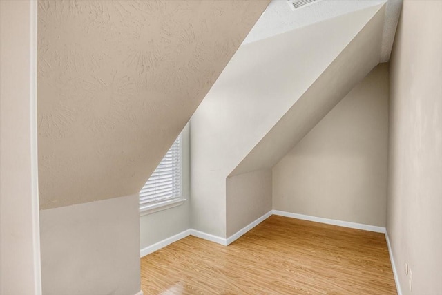 bonus room featuring lofted ceiling, a textured ceiling, baseboards, and wood finished floors