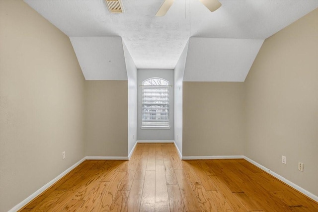 bonus room with lofted ceiling, a ceiling fan, visible vents, baseboards, and hardwood / wood-style floors