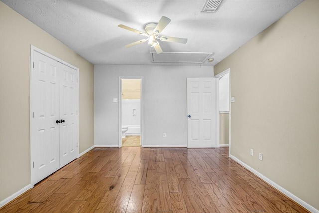 unfurnished bedroom featuring visible vents, baseboards, a closet, hardwood / wood-style floors, and attic access