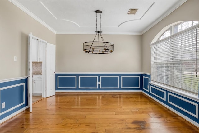 unfurnished dining area featuring a wainscoted wall, light wood-style flooring, visible vents, and crown molding