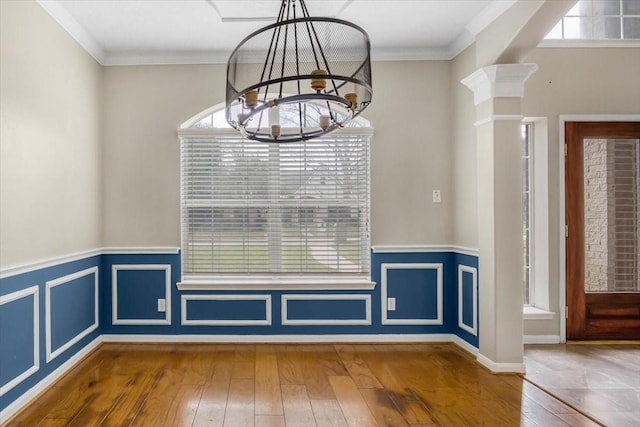 unfurnished dining area with ornamental molding, wainscoting, hardwood / wood-style flooring, and an inviting chandelier