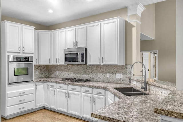 kitchen featuring decorative backsplash, light stone countertops, stainless steel appliances, white cabinetry, and a sink