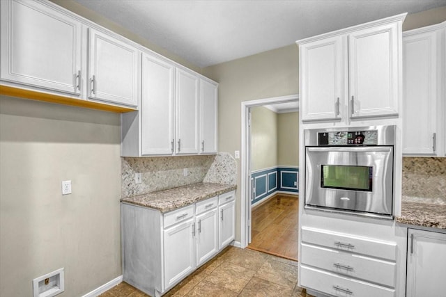 kitchen featuring tasteful backsplash, visible vents, white cabinets, light stone countertops, and oven