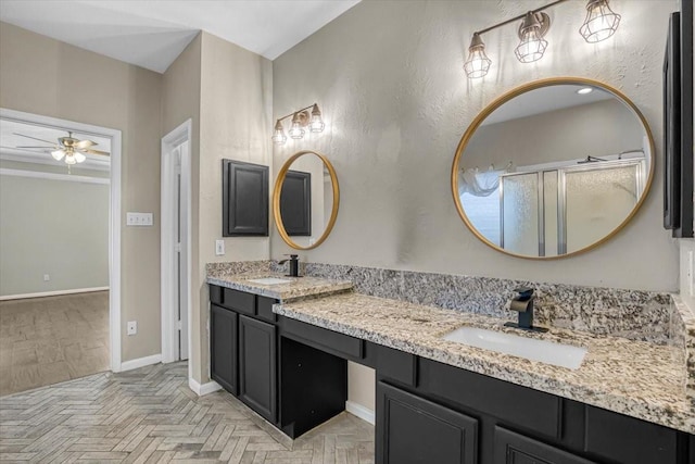 full bath with a sink, a ceiling fan, baseboards, a shower stall, and double vanity