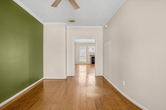 empty room with crown molding, a fireplace, visible vents, wood finished floors, and baseboards