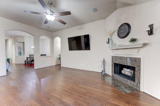 living area featuring arched walkways, visible vents, a ceiling fan, a high end fireplace, and wood finished floors