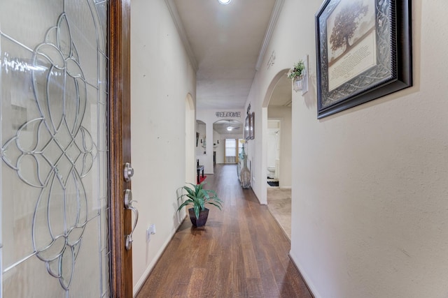 hallway with ornamental molding, arched walkways, baseboards, and wood finished floors