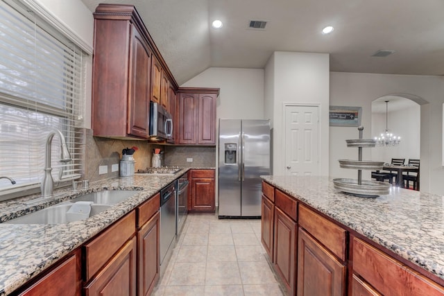 kitchen with arched walkways, stainless steel appliances, backsplash, a sink, and light stone countertops