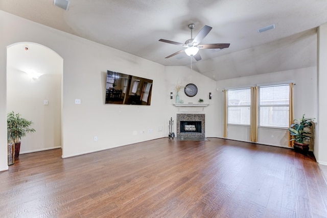 unfurnished living room with arched walkways, a fireplace with flush hearth, vaulted ceiling, ceiling fan, and wood finished floors