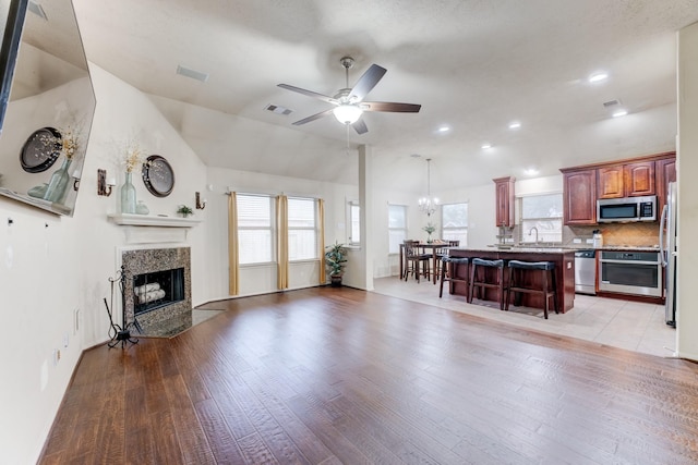 living room featuring a fireplace, light wood finished floors, lofted ceiling, visible vents, and ceiling fan with notable chandelier