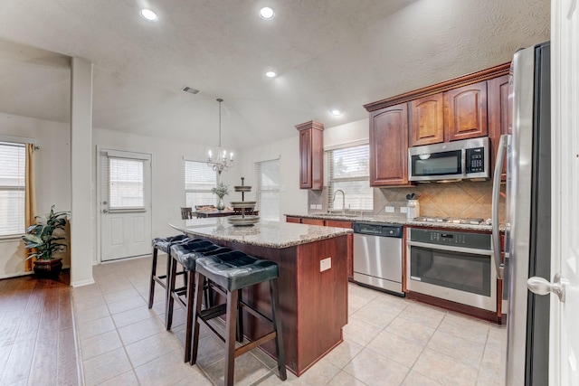 kitchen with stainless steel appliances, visible vents, decorative backsplash, a kitchen island, and light stone countertops