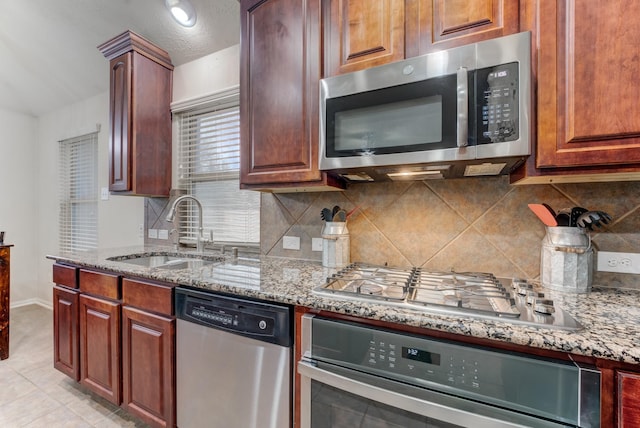 kitchen with tasteful backsplash, appliances with stainless steel finishes, light stone counters, and a sink