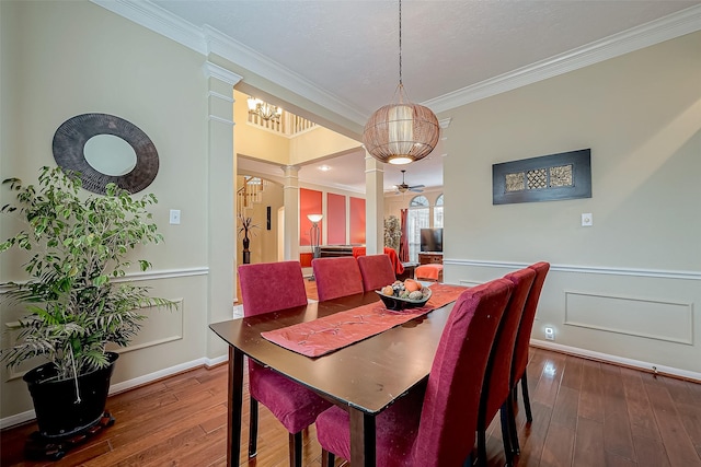 dining space with a wainscoted wall, crown molding, wood-type flooring, and decorative columns