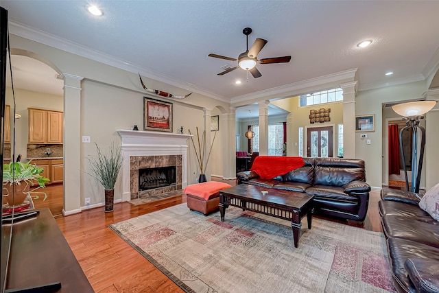 living area with light wood-type flooring, ornamental molding, a fireplace, and ornate columns