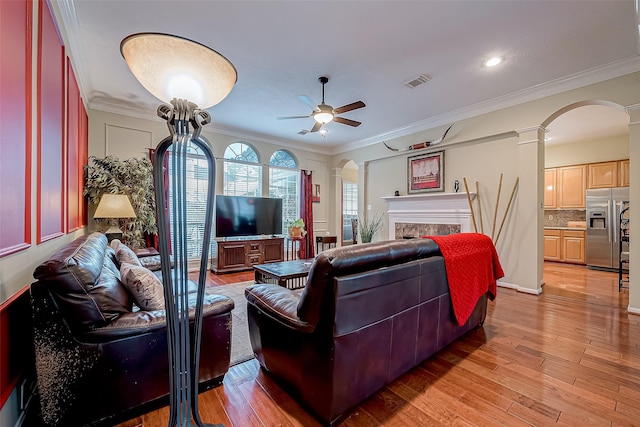 living room with a high end fireplace, visible vents, ornamental molding, light wood-style flooring, and arched walkways