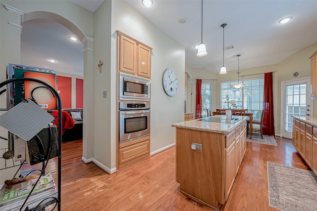 kitchen featuring light wood-style floors, a kitchen island, arched walkways, and stainless steel appliances