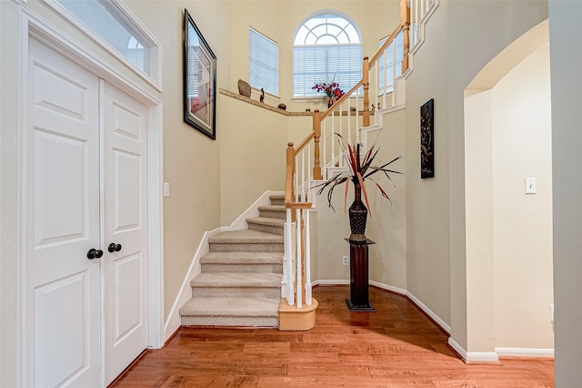 entrance foyer with wood finished floors, stairway, arched walkways, baseboards, and a towering ceiling