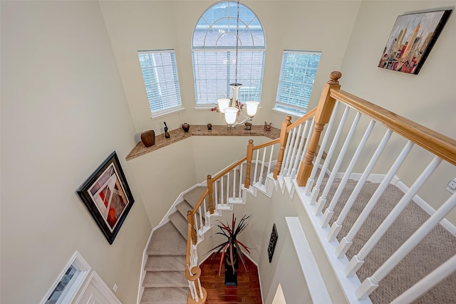 stairway with a wealth of natural light, a high ceiling, an inviting chandelier, and wood finished floors