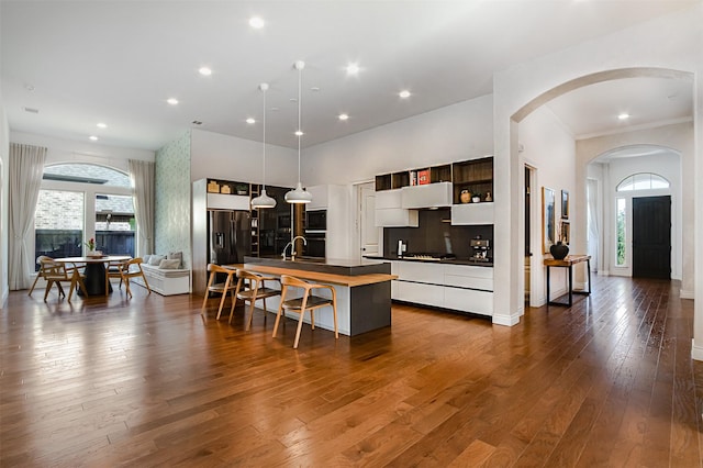 kitchen featuring an island with sink, dark wood-type flooring, black appliances, dark countertops, and a kitchen breakfast bar