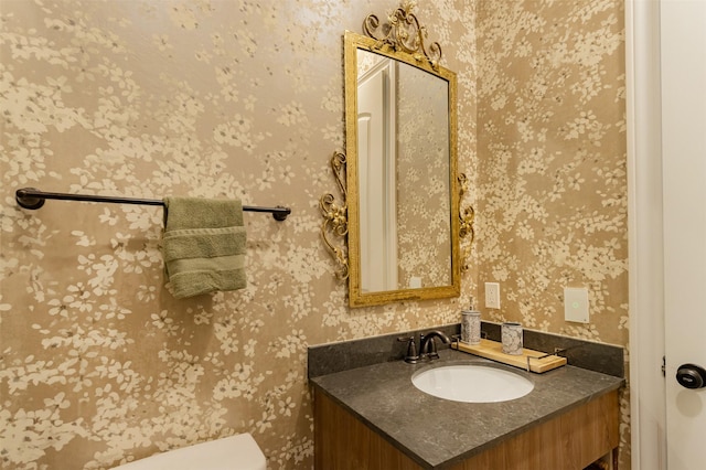 half bath with toilet, vanity, and wallpapered walls