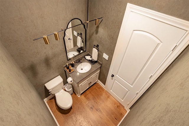 half bath with toilet, vanity, and wood finished floors