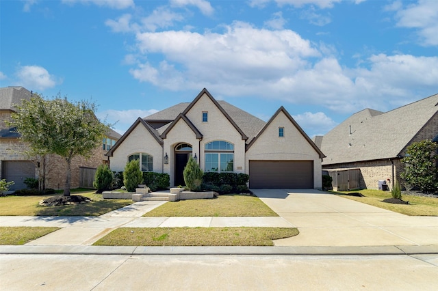 french country inspired facade with an attached garage, concrete driveway, a front lawn, and fence