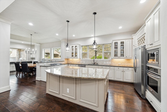 kitchen featuring dark wood-style floors, appliances with stainless steel finishes, glass insert cabinets, a peninsula, and backsplash