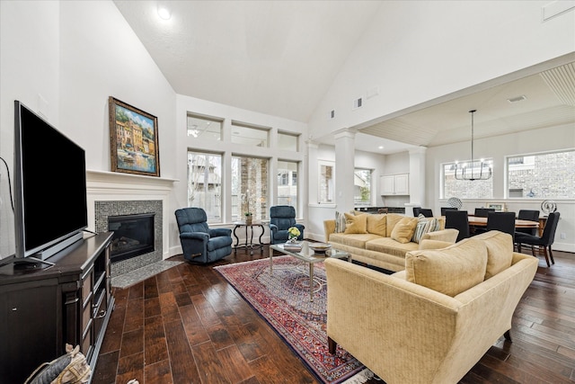 living room featuring dark wood-style floors, decorative columns, high vaulted ceiling, a chandelier, and a tile fireplace