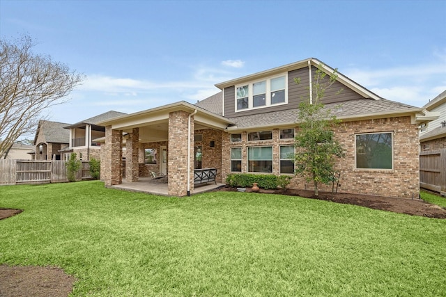 back of property with a shingled roof, a lawn, a patio, fence, and brick siding