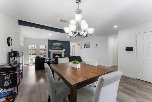 dining room featuring vaulted ceiling with beams, wood finished floors, visible vents, baseboards, and a brick fireplace