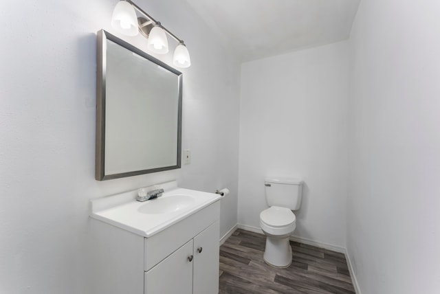 half bath featuring toilet, vanity, baseboards, and wood finished floors