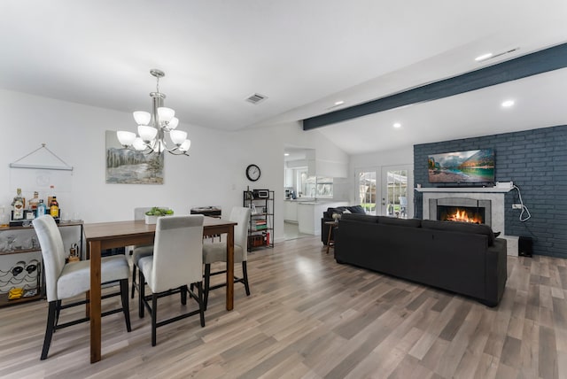 dining area with french doors, vaulted ceiling with beams, a fireplace, visible vents, and light wood-style flooring