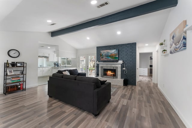 living room with visible vents, a fireplace, lofted ceiling with beams, and wood finished floors