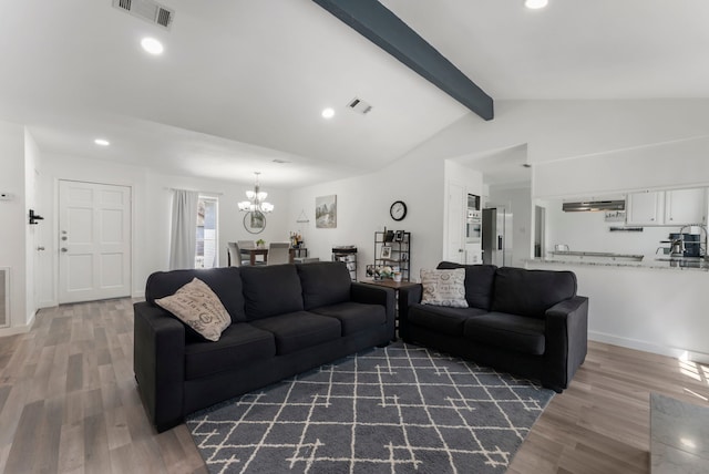 living area with lofted ceiling with beams, an inviting chandelier, visible vents, and wood finished floors