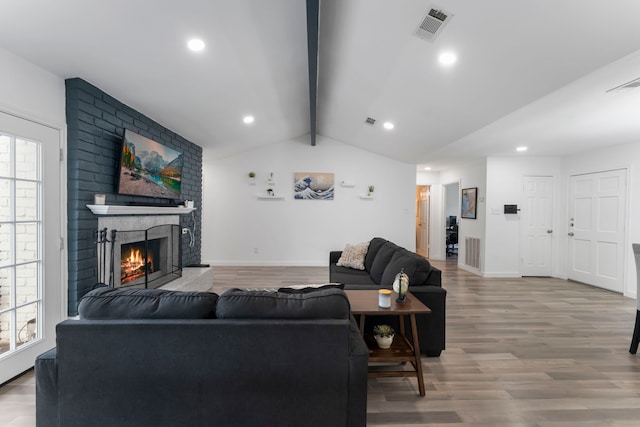 living area with a brick fireplace, visible vents, lofted ceiling with beams, and wood finished floors