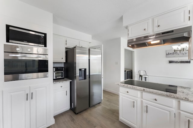 kitchen featuring stainless steel appliances, wood finished floors, white cabinets, light stone countertops, and under cabinet range hood