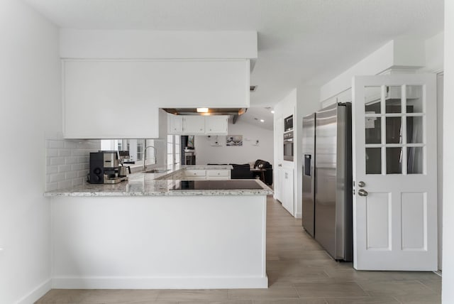 kitchen featuring light stone counters, a peninsula, white cabinetry, appliances with stainless steel finishes, and tasteful backsplash