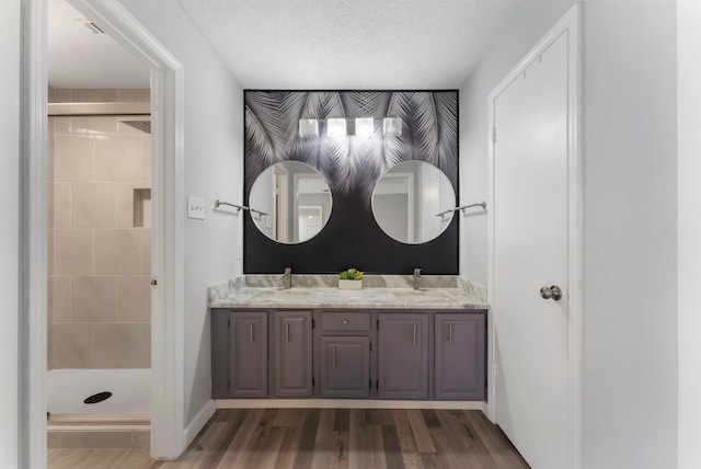 full bath with double vanity, a textured ceiling, a shower stall, wood finished floors, and baseboards