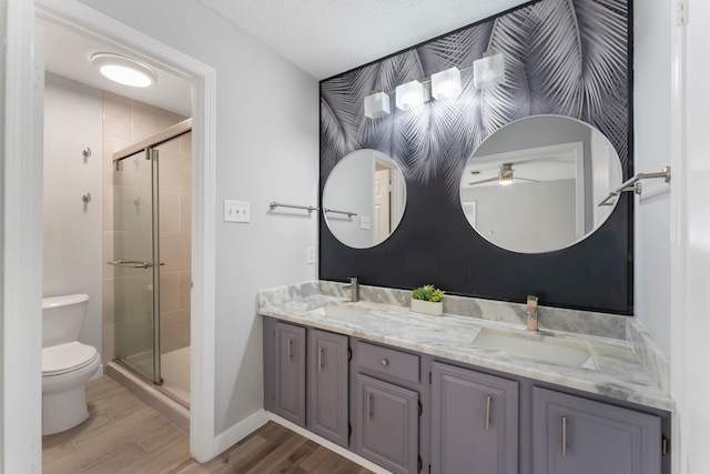 full bath featuring double vanity, toilet, wood finished floors, a shower stall, and a sink