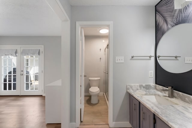 bathroom featuring french doors, toilet, wood finished floors, vanity, and a shower stall