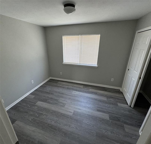 unfurnished bedroom featuring dark wood finished floors, a textured ceiling, and baseboards