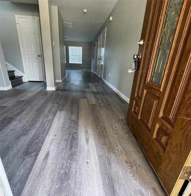 hallway with dark wood-style floors, stairway, visible vents, and baseboards