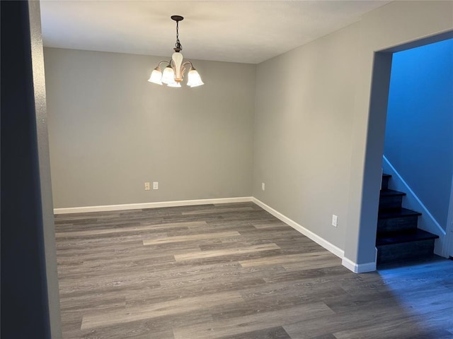 empty room featuring dark wood-style floors, stairway, a chandelier, and baseboards