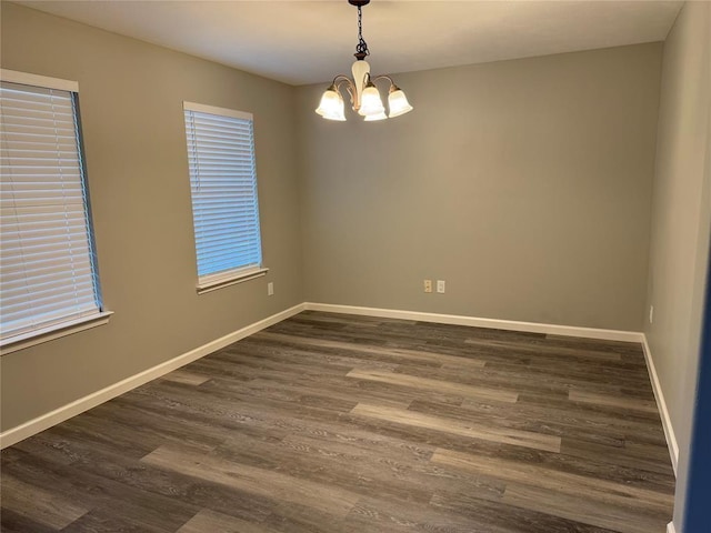 empty room featuring dark wood finished floors, a notable chandelier, and baseboards