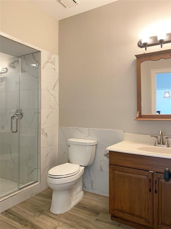 full bath with toilet, wood finished floors, vanity, tile walls, and a marble finish shower