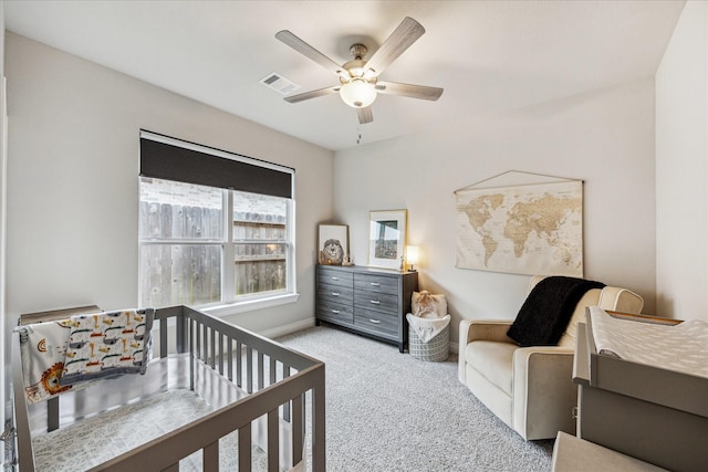 carpeted bedroom with ceiling fan, a nursery area, visible vents, and baseboards