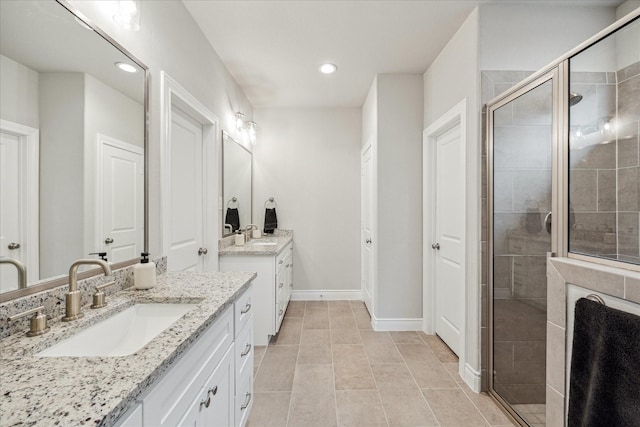 bathroom with a stall shower, two vanities, a sink, and baseboards