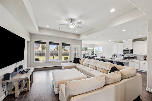 living room featuring recessed lighting, ceiling fan with notable chandelier, dark wood-style flooring, visible vents, and a tray ceiling