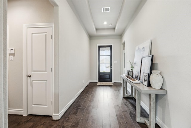 foyer entrance featuring dark wood-type flooring, a tray ceiling, visible vents, and baseboards