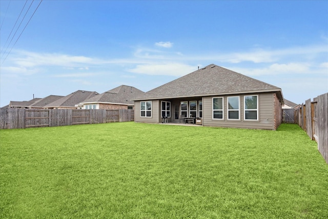 rear view of property featuring a yard, roof with shingles, a patio area, and a fenced backyard